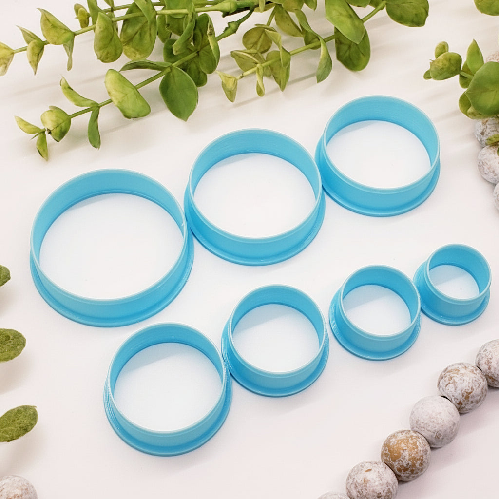 Set of blue circular clay cutters on a white surface with greenery
